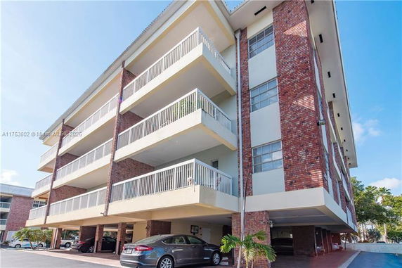 Front view of a multi-story building with balconies and parking underneath.
