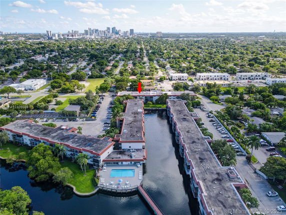 Aerial view of large canal-side residential buildings with parking areas, pool, and cityscape in the background.