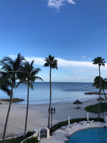 View of a beach with palm trees and a poolside area.