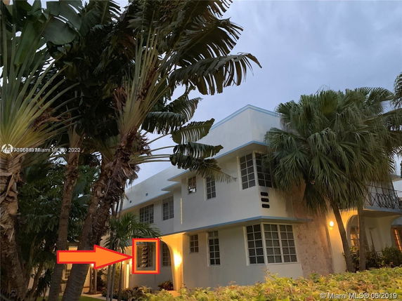 Front view of a two-story building with prominent windows and tropical plants.