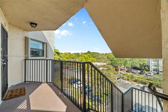 Balcony with railing overlooking a parking area and greenery.