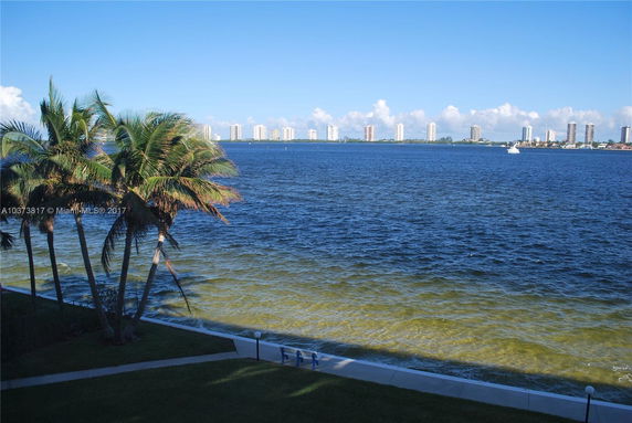 View of a waterfront area with palm trees and buildings across the water.