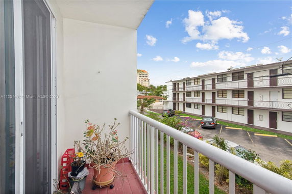View from a balcony overlooking a parking area and a multi-story residential building.