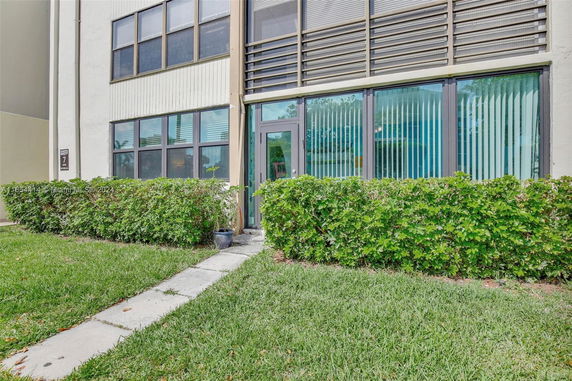 Front view of a building with large windows and a door, surrounded by greenery.