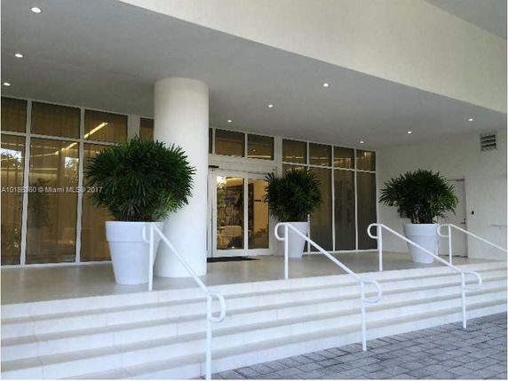 Front view of a building entrance with steps, large potted plants, and a glass door.