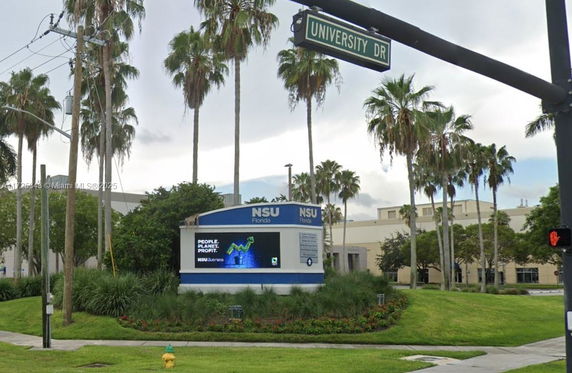 Front view of a large institutional building with prominent signage, surrounded by palm trees.