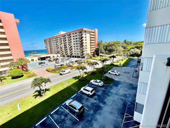 View from a building showing multi-story residential buildings near the ocean and a parking area.
