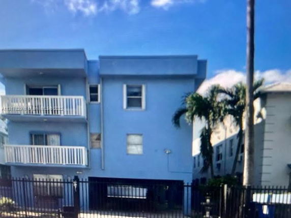 Front view of a multi-story building with balconies and a gated entrance.