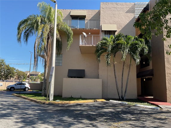 Front view of a multi-story building with balconies and palm trees.