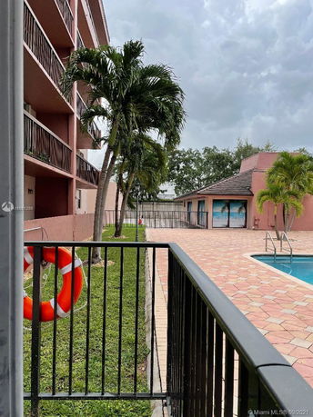 Side view of a multi-story building with balconies, adjacent to a pool area.