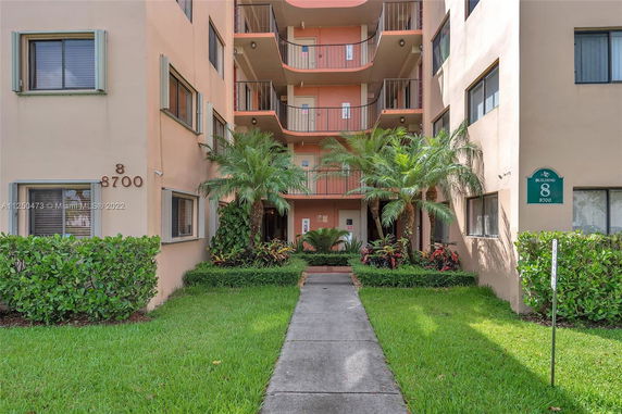 Front view of a multi-story building with balconies and a landscaped entrance.