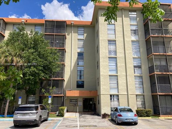 Front view of a multi-story apartment building with balconies and parked cars below.