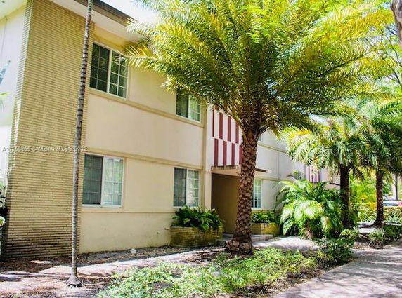 Front view of a two-story house with large windows and surrounding palm trees.