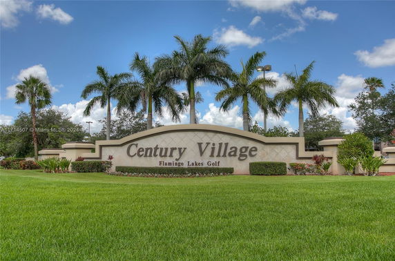 Entrance sign of Century Village, Flamingo Lakes Golf, with palm trees in the background.