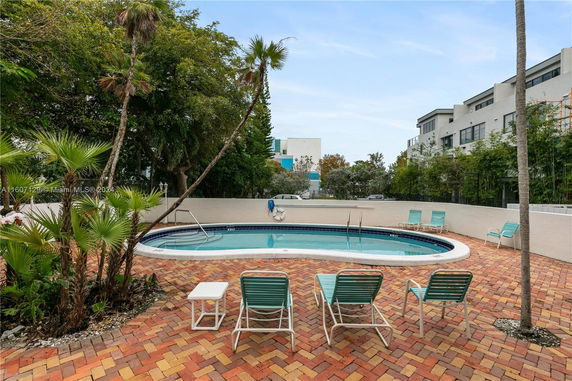 Outdoor swimming pool with lounge chairs, surrounded by brick flooring and lush greenery.