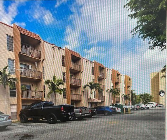 Front view of a multi-story apartment building with balconies and parking area.
