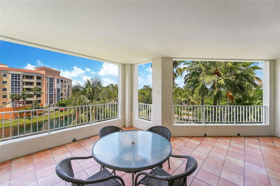 Outdoor patio area with glass table and chairs overlooking trees and nearby buildings.