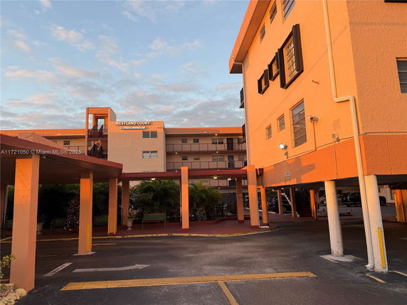 Front view of a multi-story condominium building with a walkway and parking area.