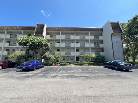 Front view of a multi-story apartment building with balconies and surrounding parking area.
