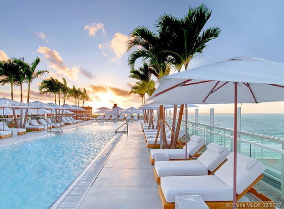 Outdoor swimming pool area with lounge chairs and umbrellas overlooking the ocean.