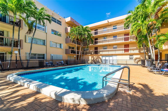 Outdoor area with a rectangular swimming pool surrounded by a multi-story building.