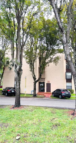 Front view of a multi-story residential building with parked cars.