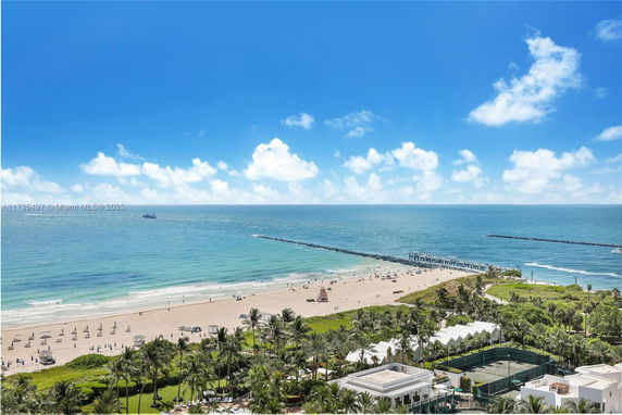Panoramic view of a beach and ocean with a pier and surrounding greenery.
