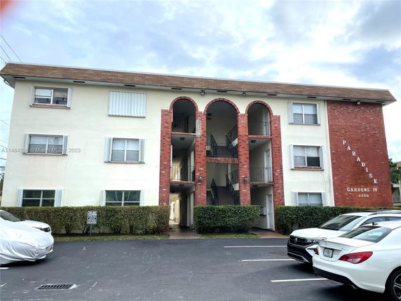 Front view of a three-story apartment building with brick arches and parking area.