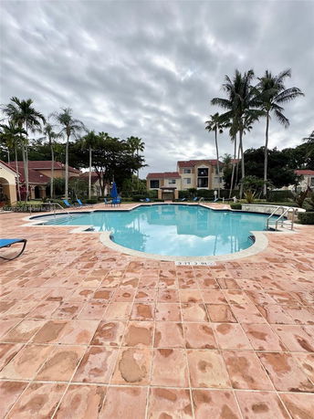 Outdoor swimming pool with surrounding buildings and palm trees.