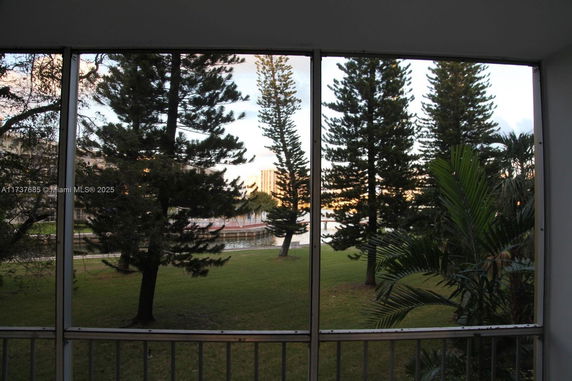 View through a screened window showing trees and a water body with distant buildings.