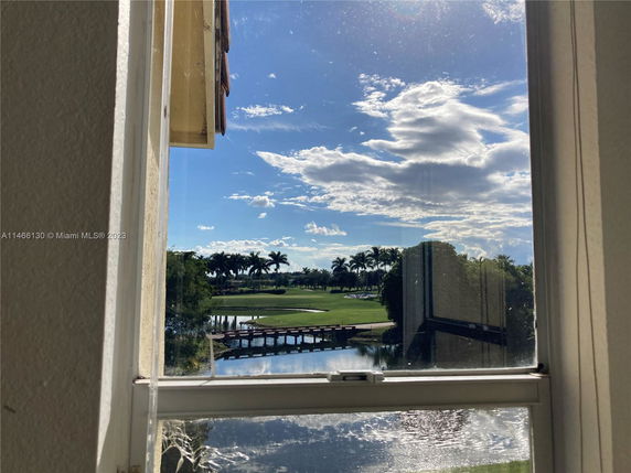 View from a window showing a golf course, water body, and palm trees under a sky with clouds.