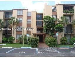 Front view of a multi-story residential building with balconies and surrounding plants.