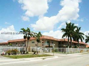Front view of a two-story building with a fence and palm trees.