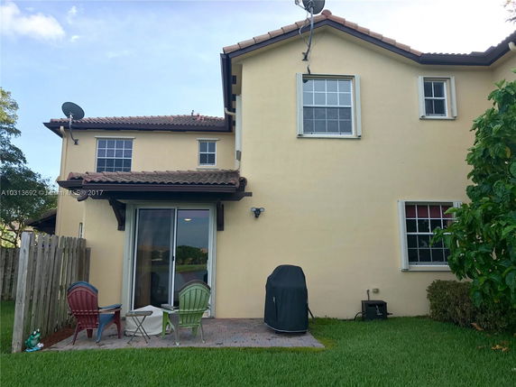 Rear view of a two-story house with patio chairs and a barbecue grill.