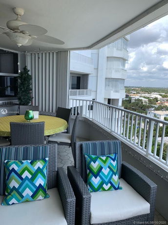 Elevated balcony view with outdoor seating and decorative pillows, overlooking surrounding buildings and landscape.