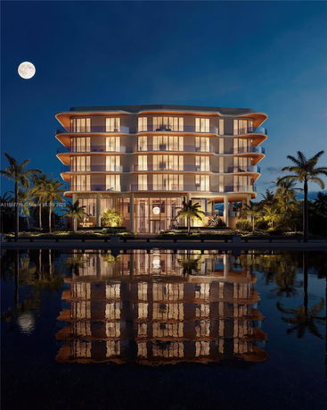 Night view of a multi-story building with illuminated windows and a water reflection in front.