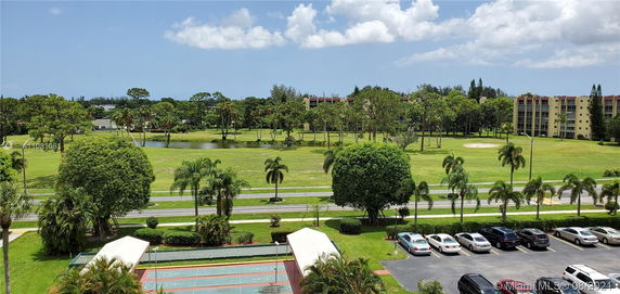 View of surrounding green area with trees and a small pond, seen from a building with a parking area below.