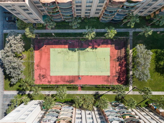 Top view of an outdoor play area with a tennis court surrounded by greenery and buildings.