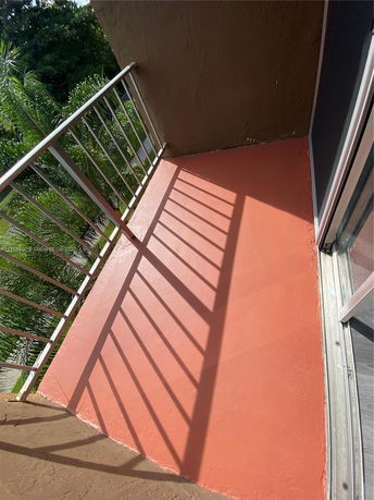 Small outdoor balcony with red flooring and metal railing.