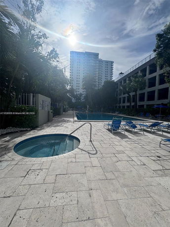 Outdoor swimming pool area with sun loungers and a tall building in the background.
