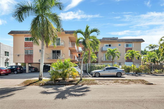 Front view of a three-story apartment building with balconies and covered parking area.