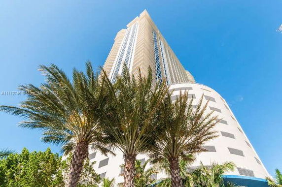 Front view of a tall, modern high-rise building with palm trees at the base.