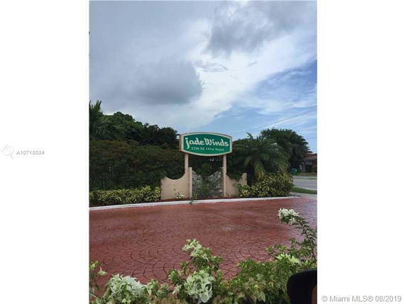 Entrance sign for Jade Winds with surrounding greenery.