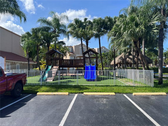 Outdoor playground with slides and climbing structures surrounded by palm trees.