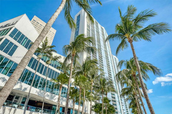 Front view of a tall modern building with large windows and palm trees.