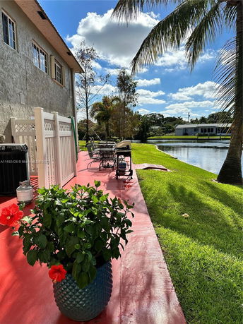 Side view of a house next to a canal with outdoor furniture and palm trees.