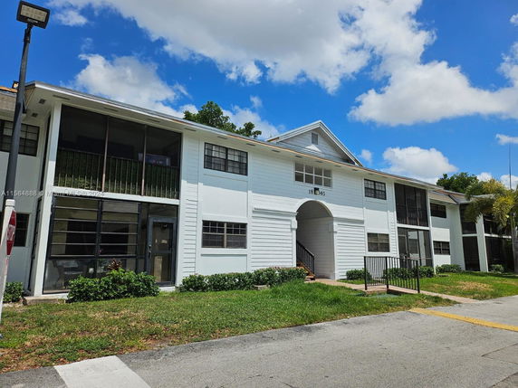 Front view of a multi-story residential building with white siding and balconies.