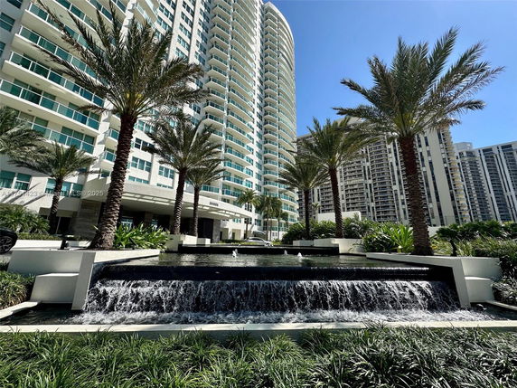 Front view of a modern high-rise building with palm trees and a water feature.