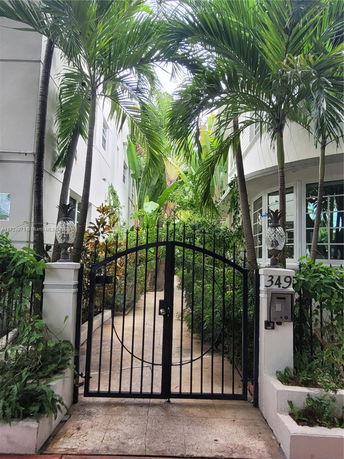 Front view of a gated entrance to a house with tropical landscaping.
