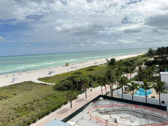 Panoramic view of a beach and ocean with nearby palm trees and buildings.